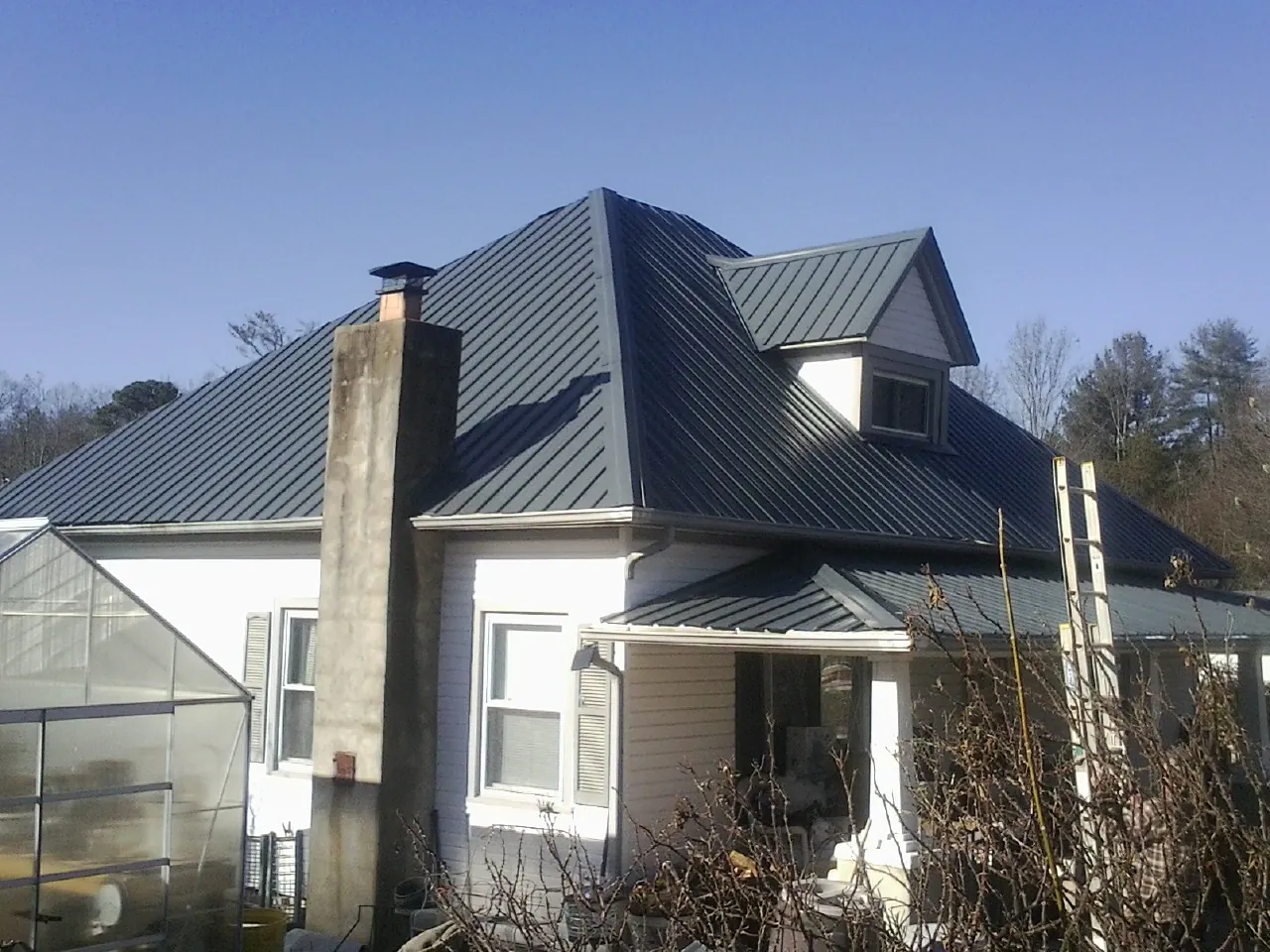 Dark blue standing seam metal roof on a white farmhouse with dormer — Slate & Tile Roof Repair by Roofing Brothers in Tuckahoe