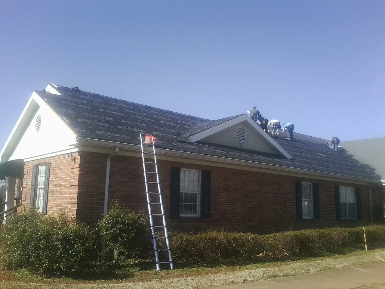Crew tearing shingles off a brick ranch roof with a ladder set — Emergency Roof Repair work by our crew in Tuckahoe