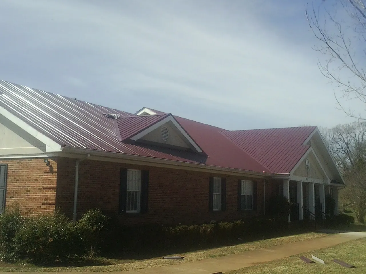 Red metal roof with gabled entries on a long brick building, from a Hail Damage Roof Repair job in Tuckahoe