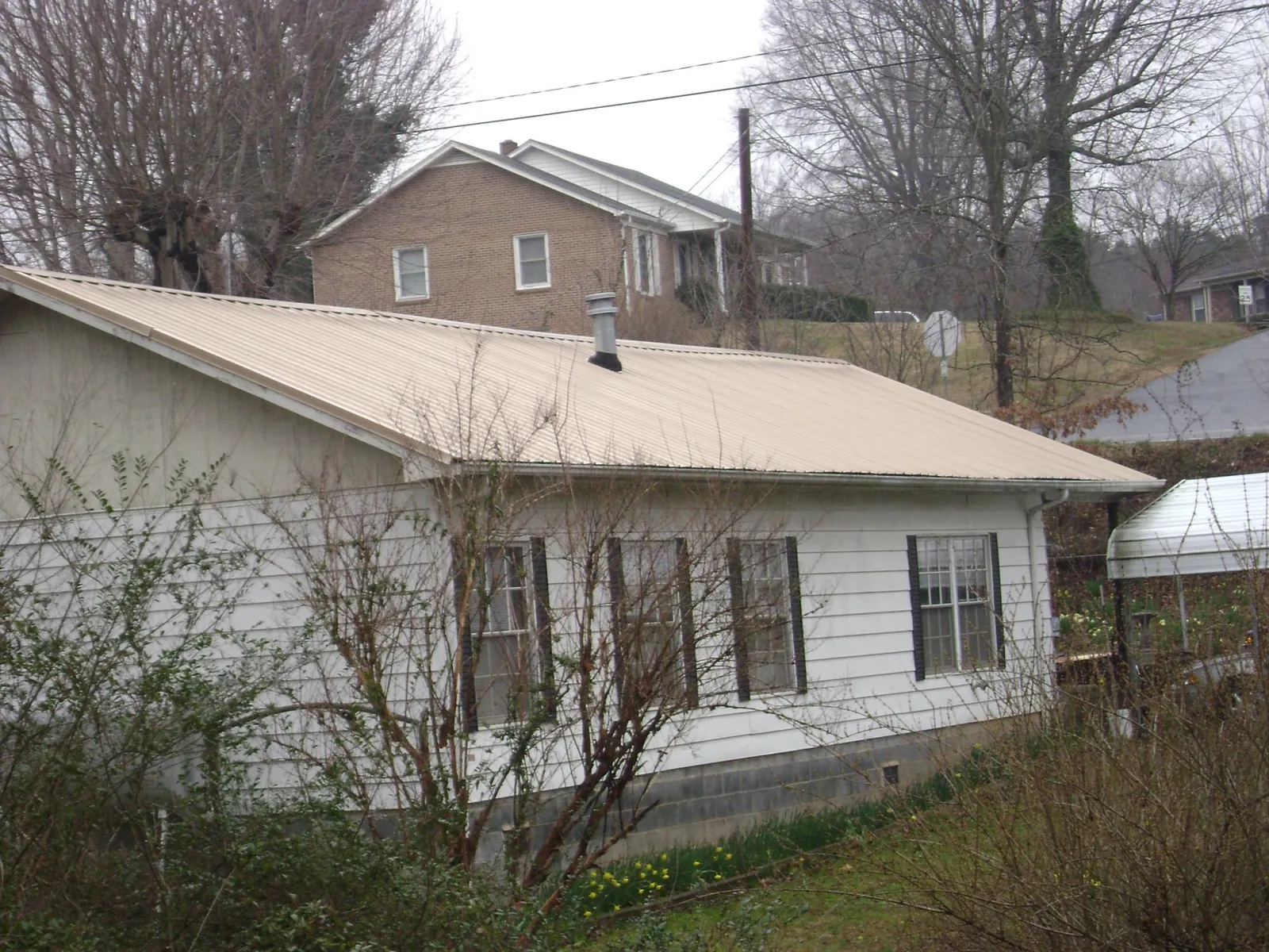 Tan metal roof on a white sided house set into a hillside — Commercial Roofing by Roofing Brothers in Tuckahoe